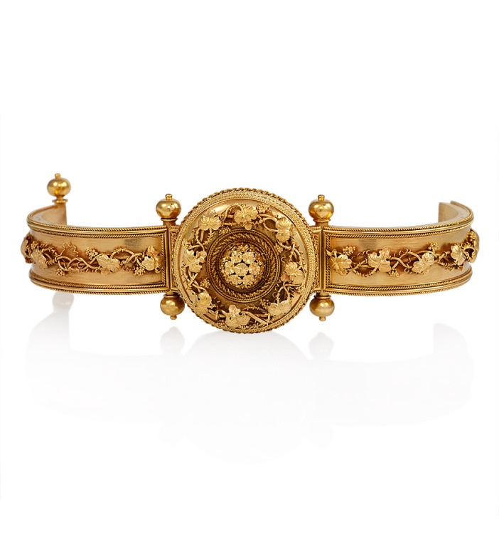 An 18K antique bangle in the style of Castellani, with a central panel and appli...