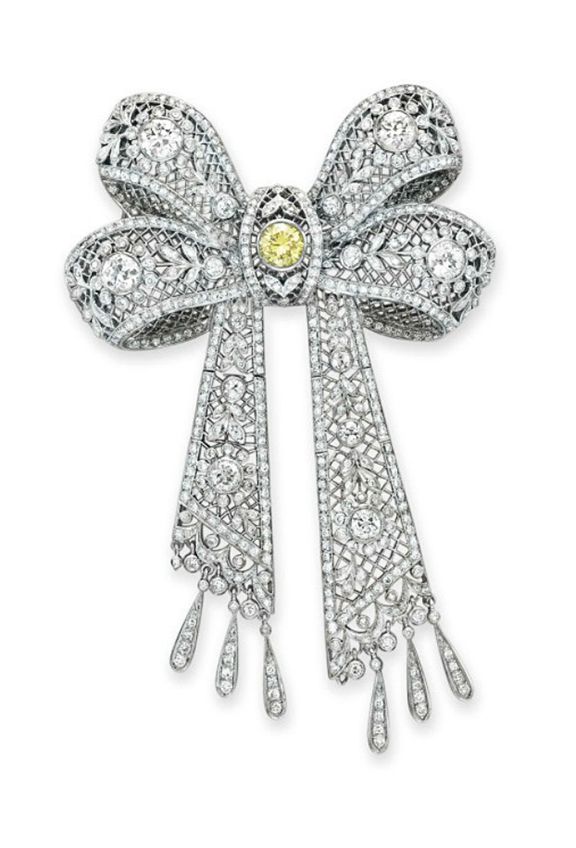 A DIAMOND AND COLORED DIAMOND BOW BROOCH  Designed as an openwork circular and o...